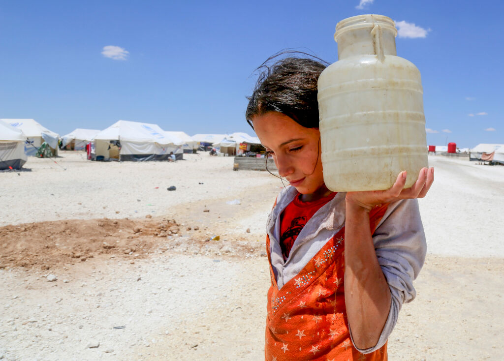 Syyrian maansisäinen pakolainen, 12-vuotias Horriya kantaa vettä jerrykannussa Ain Issan epävirallisella pakolaisleirillä lähellä Raqqan kaupunkia vuonna 2017. UNICEF huolehti alueen pakolaisten vesihuollosta mm. kuljettamalla päivittäin lähes miljoonaa litraa puhdasta vettä rekoilla.