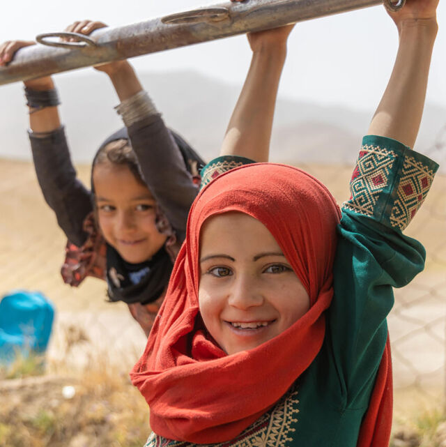 Två lågstadiebarn från Afganistan gungar i en klätterställning.