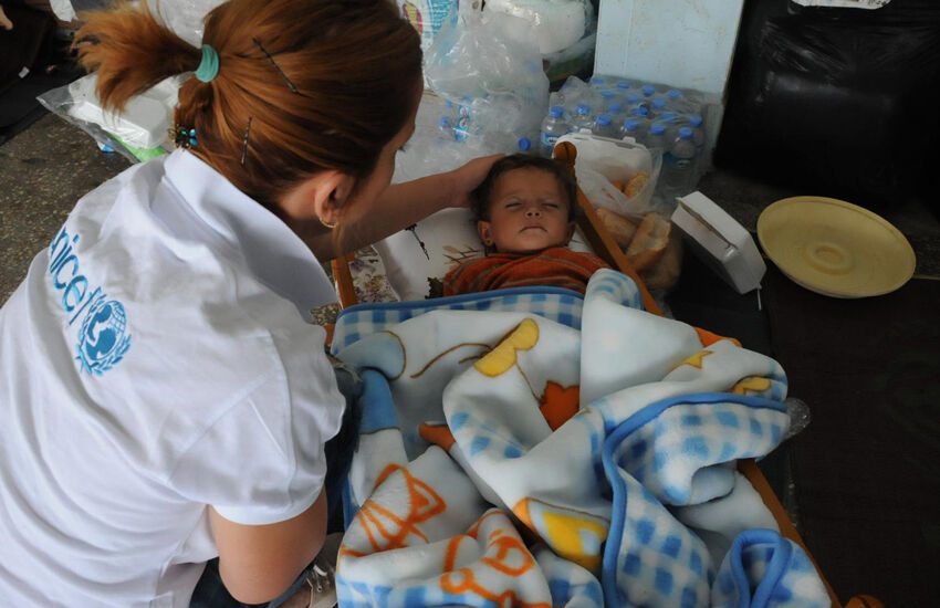 UNICEFin työntekijä tarkistaa nukkuvan lapsen kunnon pakolaiskeskukseksi muuttuneessa koulussa Suruçin alueella Turkissa, lähellä Syyrian rajaa.