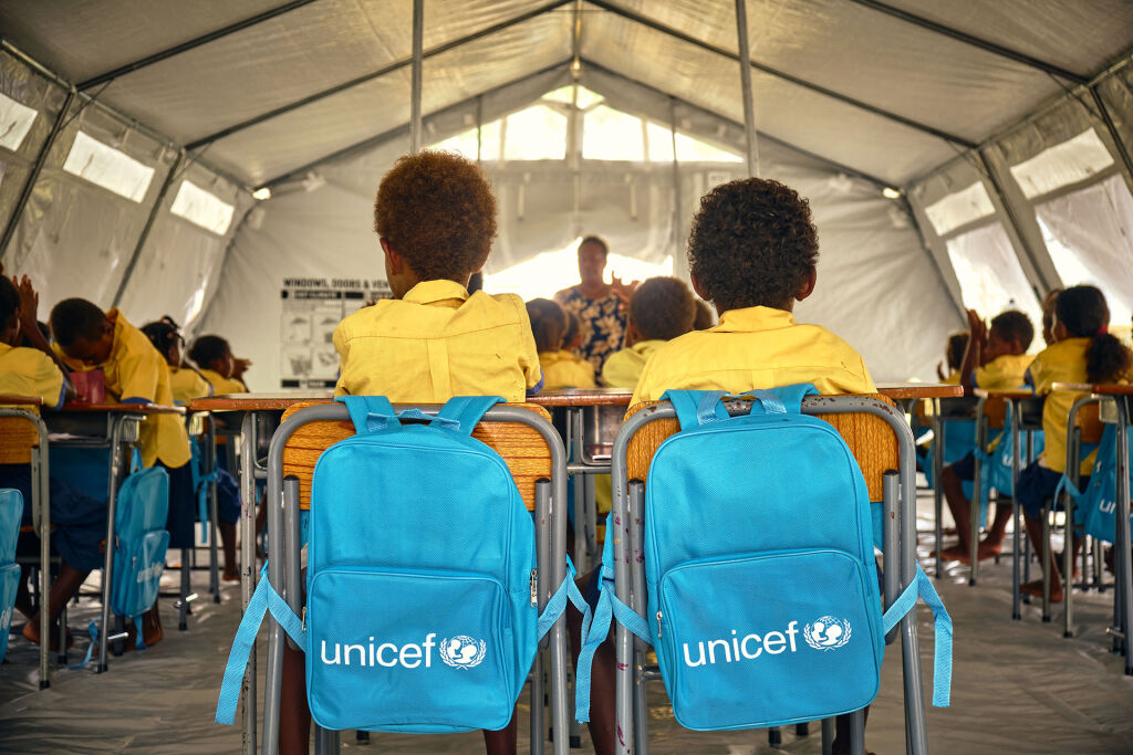 Kaksi koululaista istuu vierekkäin telttakoulussa. Tuolin selkänojilla UNICEF-reput.