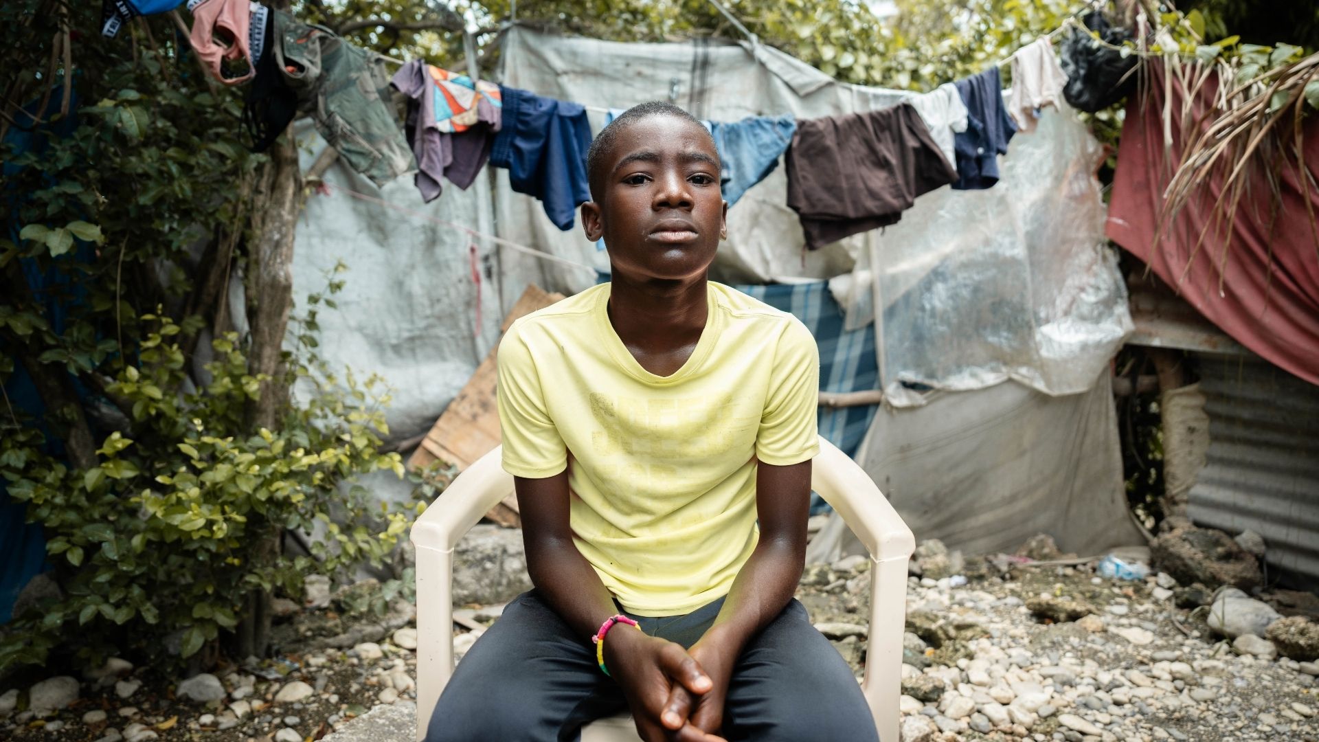 Haitilainen poika istuu tuolilla keskellä telttakylää.