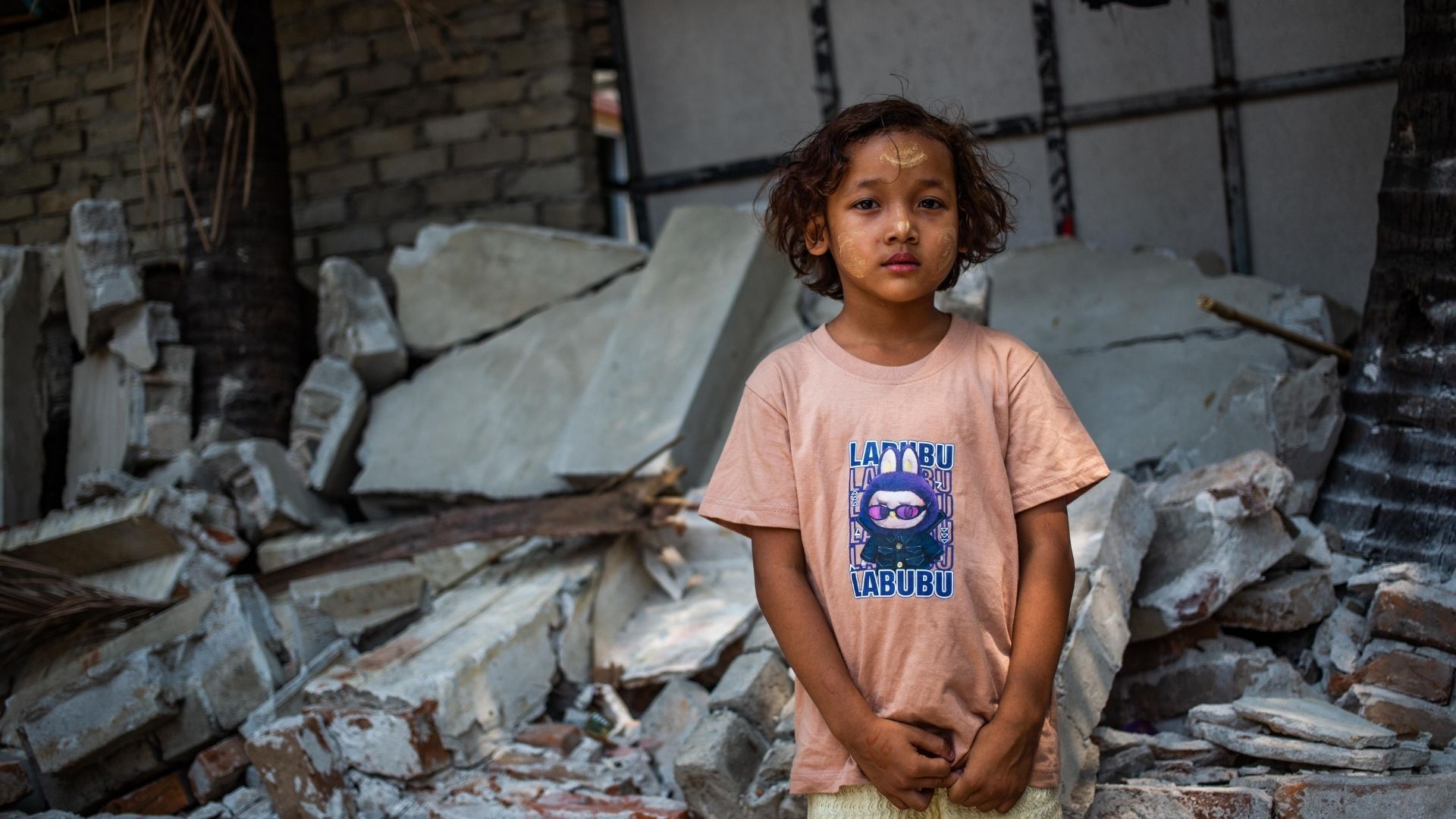 Myanmarilainen tyttö maanjäristyksessä tuhoutuneen rakennuksen edessä.