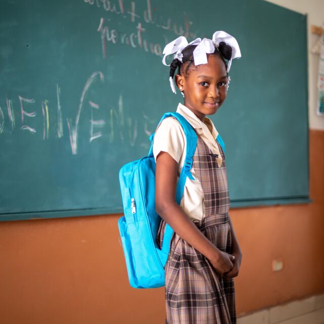 Lapsi luokan edessä UNICEF-reppu selässään.