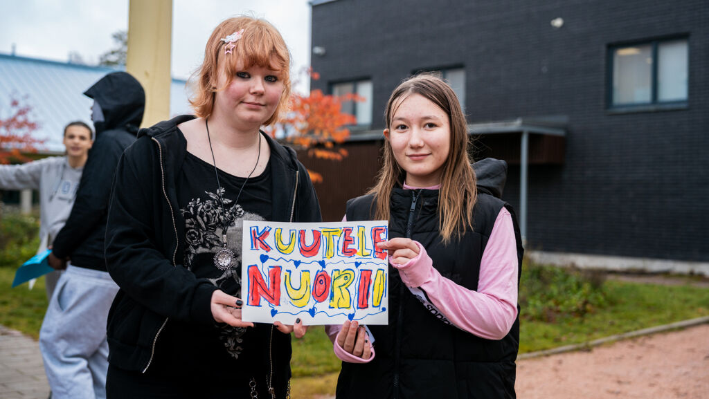 Kaksi yläkoululaista pitelee kylttiä, jossa lukee "Kuuntele nuorii".