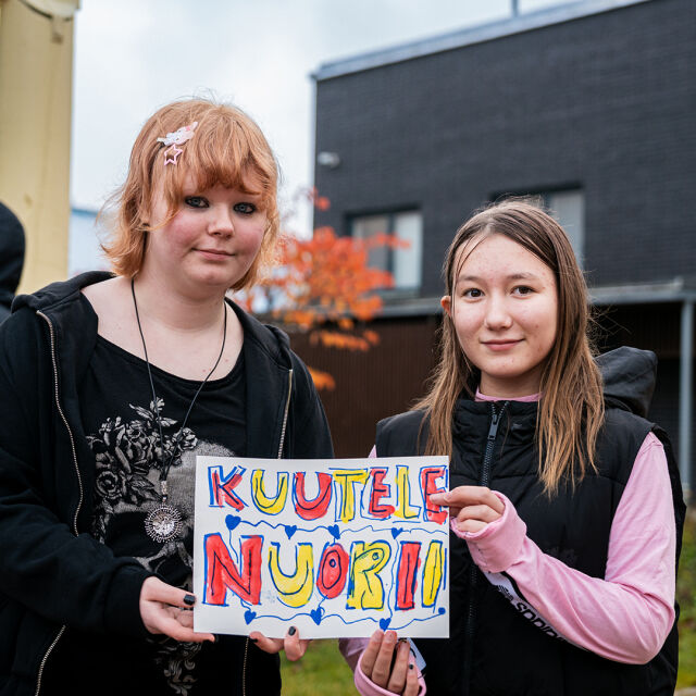 Kaksi yläkoululaista pitelee kylttiä, jossa lukee "Kuuntele nuorii".