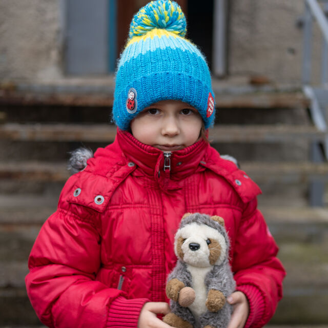 Punaiseen toppatakkiin ja siniseen tupsupipoon pukeutunut lapsi pitelee majavapehmolelua rakennuksen edessä.