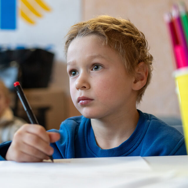 Siniseen paitaan pukeutunut lapsi piirtää pöydän ääressä.