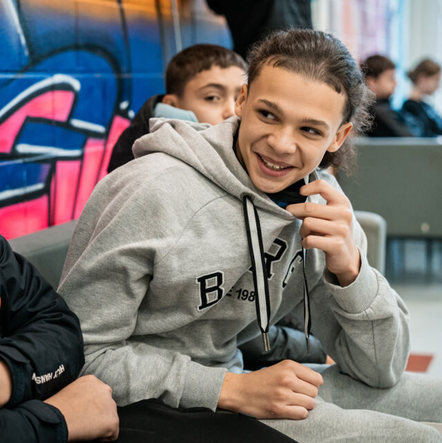 Yläkouluikäinen nuori istuu kavereidensa keskellä koulun käytävällä.