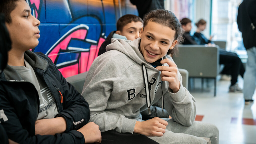 Yläkouluikäinen nuori istuu kavereidensa keskellä koulun käytävällä.