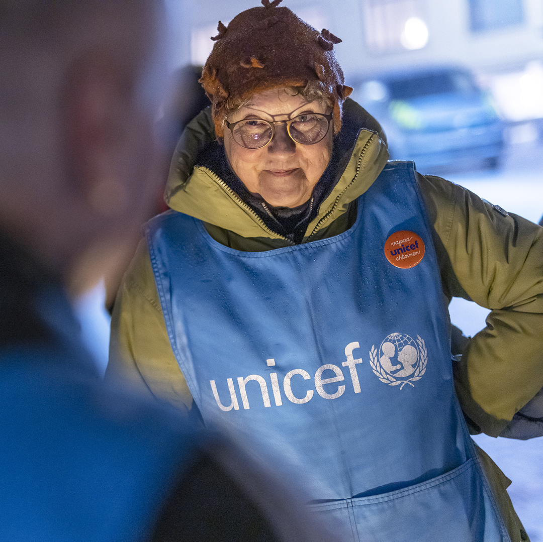 UNICEF-vapaaehtoinen keskustelee asiakkaan kanssa UNICEF-liivi yllään.