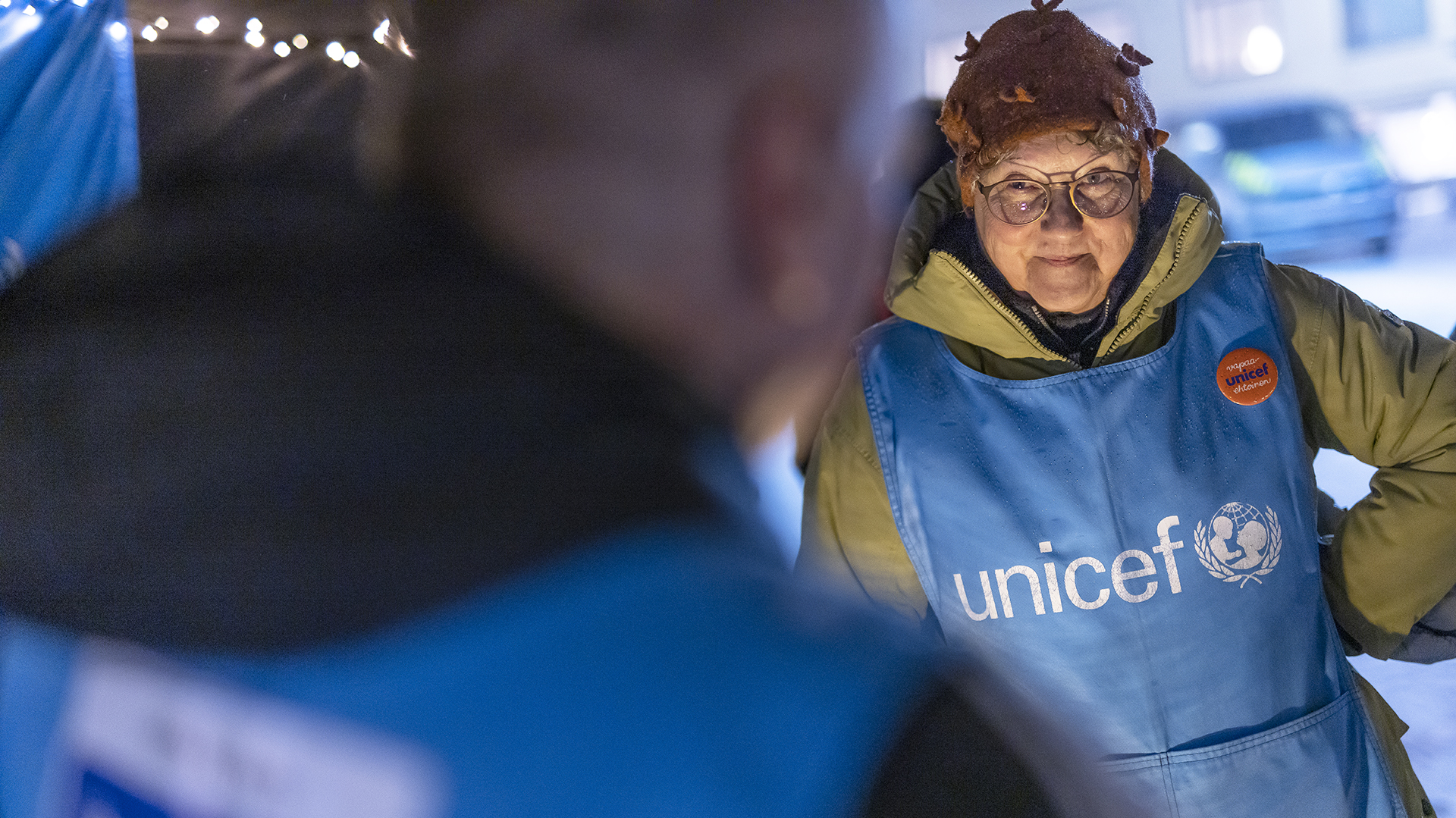 UNICEF-vapaaehtoinen keskustelee asiakkaan kanssa UNICEF-liivi yllään.