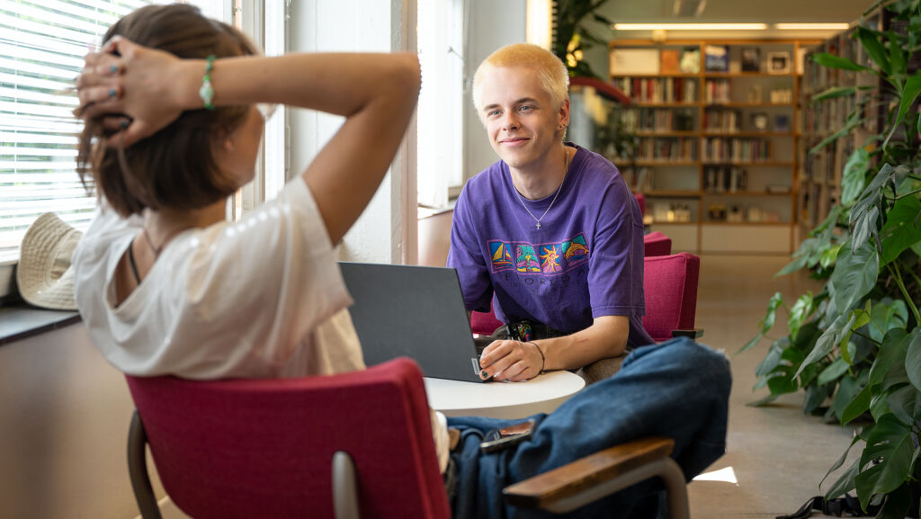 Kaksi nuorta istuu tietokoneilla kirjastossa.