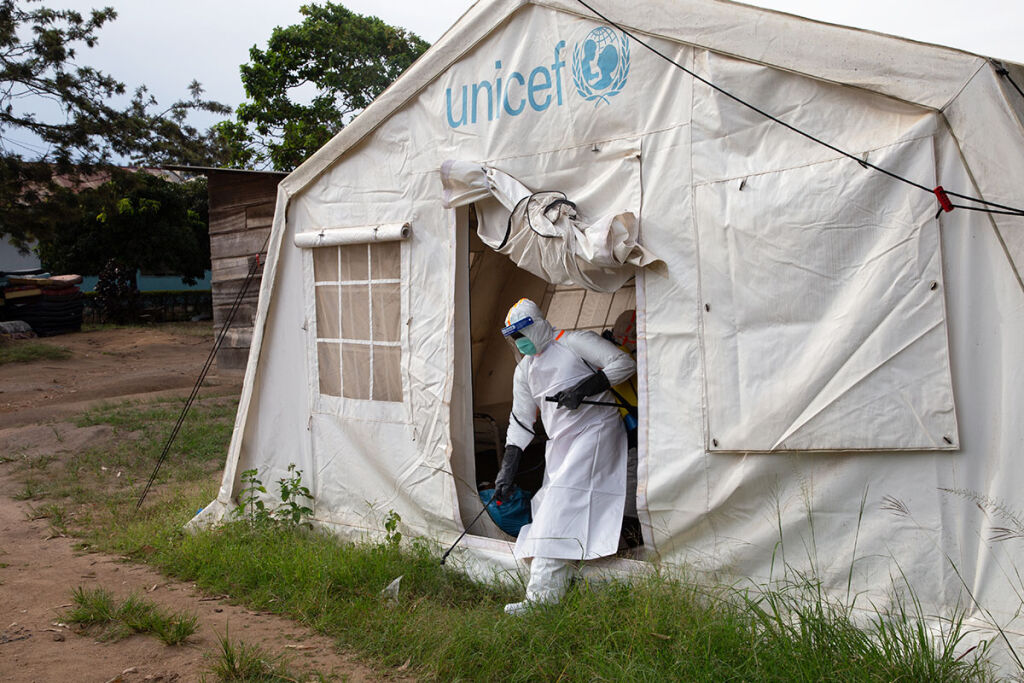Työntekijä desinfioi UNICEFin klinikkateltan edustaa ebola-suojavarustus päällään.