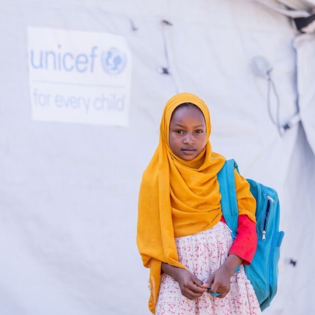 Lapsi UNICEF-teltan edessä koulureppu selässään.