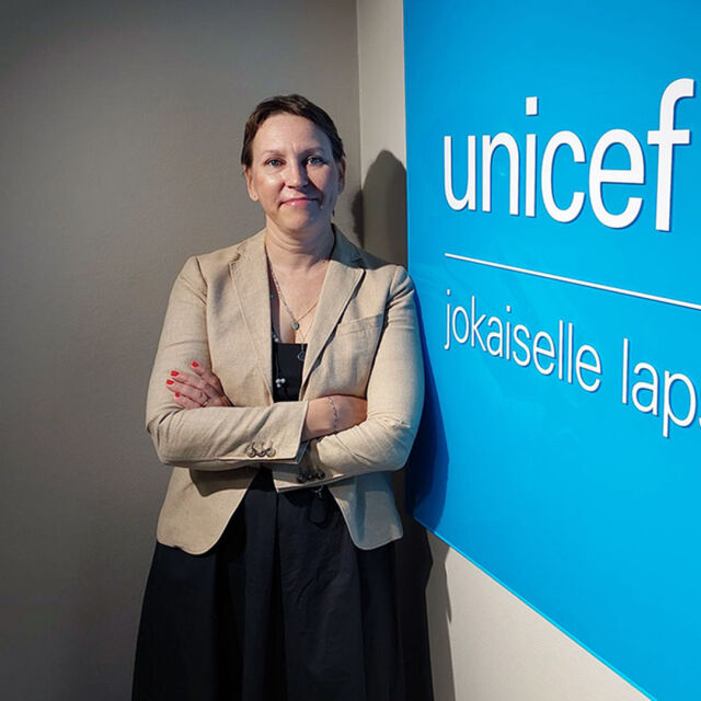 Mirkka Mattila nojaa UNICEFin logoseinään.