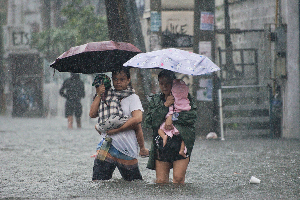 Kaksi aikuista kahlaa tulvavedessä lapset sylissä.