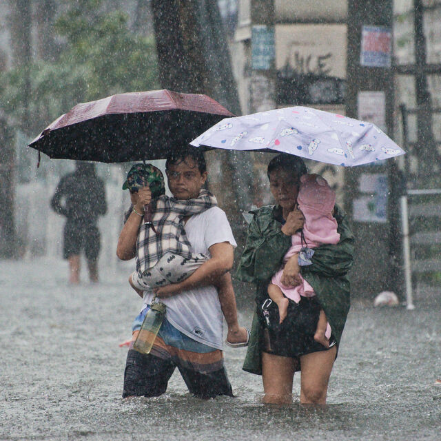 Kaksi aikuista kahlaa tulvavedessä lapset sylissä.