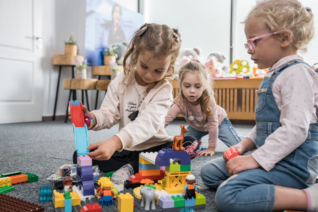 Päiväkoti-ikäinen lapsi rakentaa legoista liukumäkea, vierellä istuu polvillaan toinen lapsi ja taustalla näkyy kolmas lapsi.