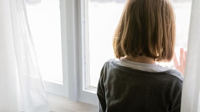 Lapsi seisoo ikkunan edessä ja katsoo ulos.