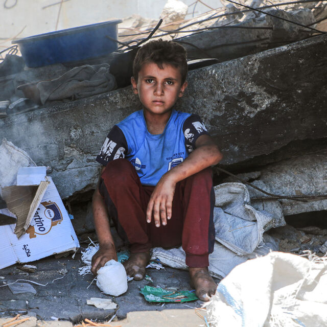 Gazalainen lapsi istuu ja katsoo vakavana kameraan keskellä raunioita.
