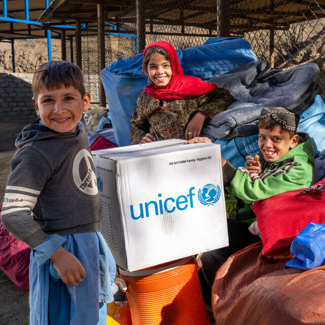 Kolme lasta nauravat keskellään pahvilaatikko, jossa UNICEFin logo.