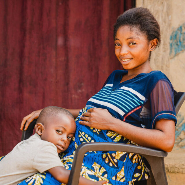 Raskaana oleva nainen istuu tuolissa ja pieni lapsi halaa häntä.