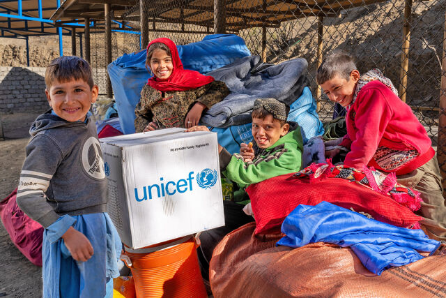 Neljä lasta nauravat keskellään pahvilaatikko, jossa UNICEFin logo. 