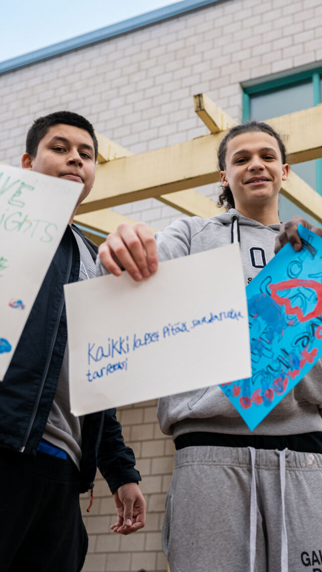 Kolme nuorta seisoo Suomessa koulun pihalla ja pitää käsissään itse tekemiään kylttejä, jossa he kertovat lapsen oikeuksista. 