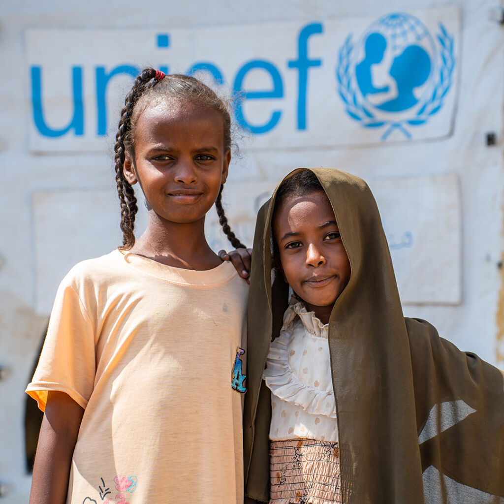 Kaksi lasta teltan edessä, jossa lukee UNICEF.