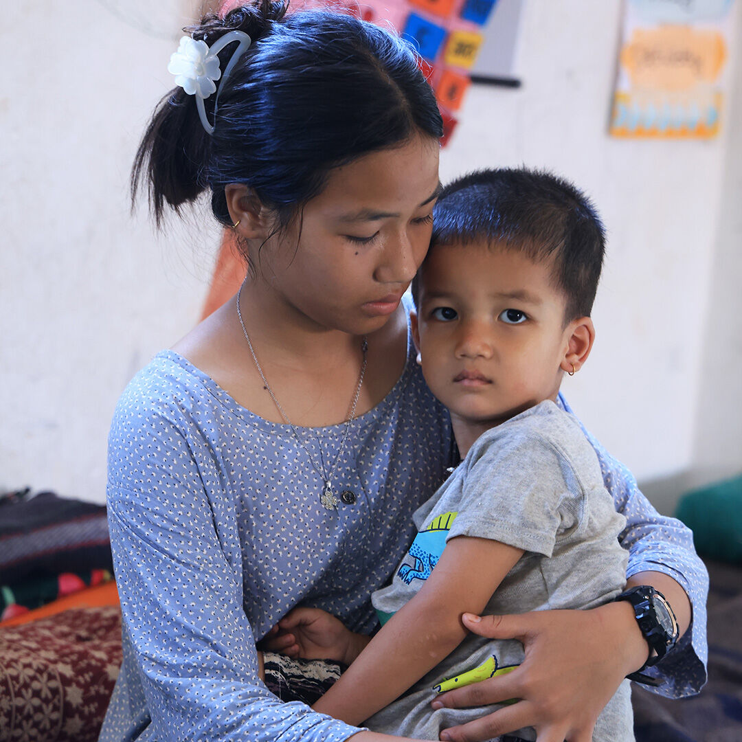 Aikuinen pitää sylissään lasta, joka katsoo vakavana kameraan Nepalissa.