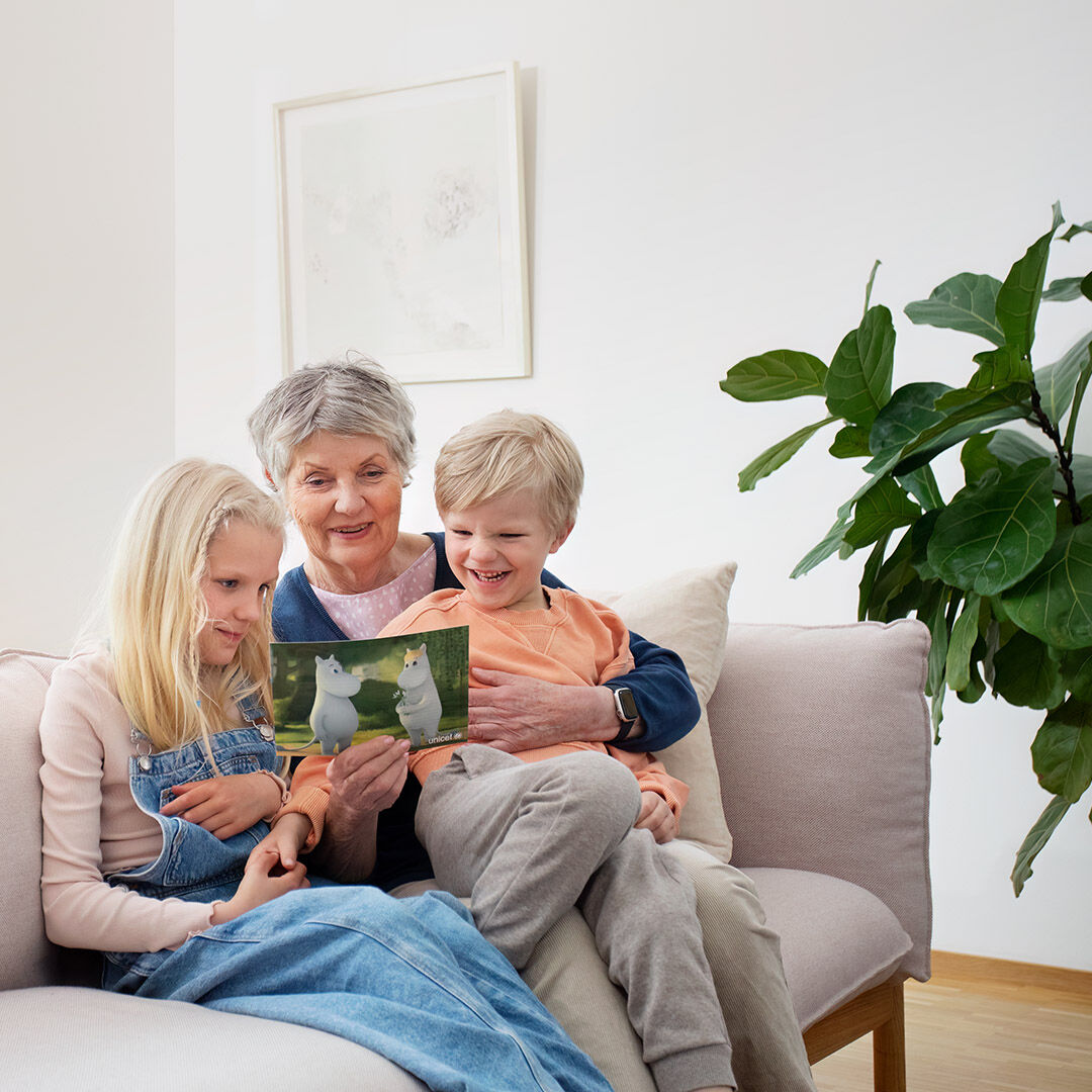 Mummo ja lapsenlapset katselevat yhdessä Muumien seikkailupostin sisältöä.