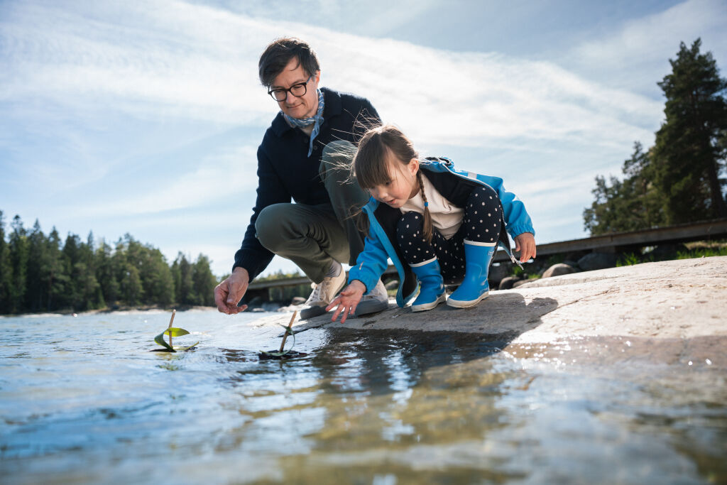 Lapsi ja aikuinen leikkivät rannassa kaarnalaivalla.