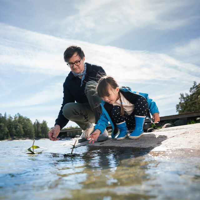 Lapsi ja aikuinen leikkivät kaarnalaivalla veden äärellä.