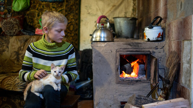 Lapsi pitää sylissään kissaa ja lämmittelee hellan ääressä Ukrainassa.