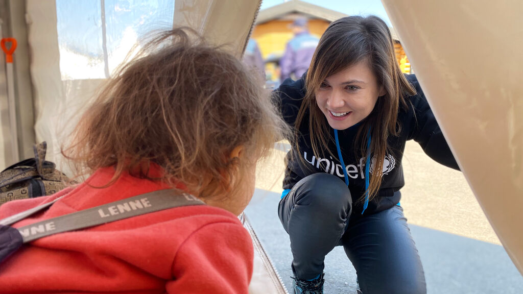 UNICEFin työntekijä kurkistaa telttaan, jossa on lapsi. 