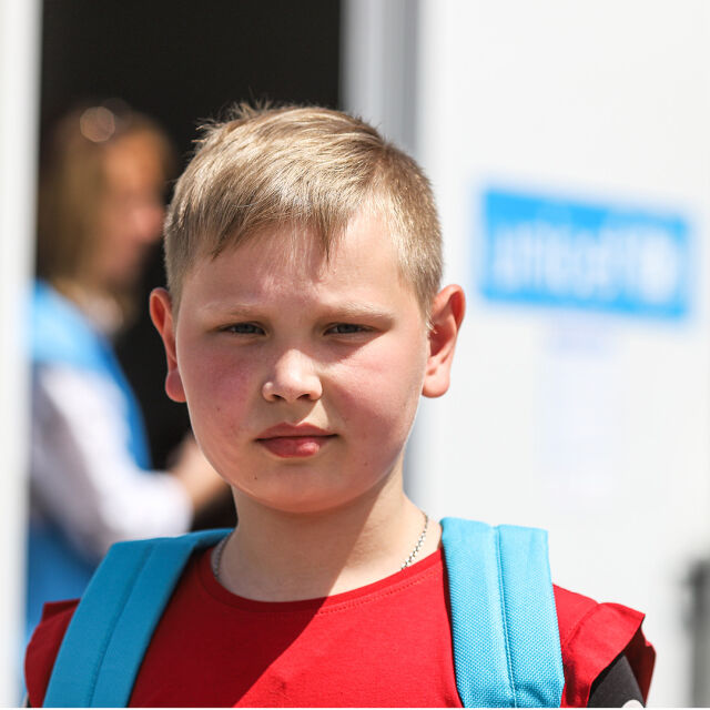 Lapsi katsoo kameraan, hänellä on UNICEF-koulureppu selässään.