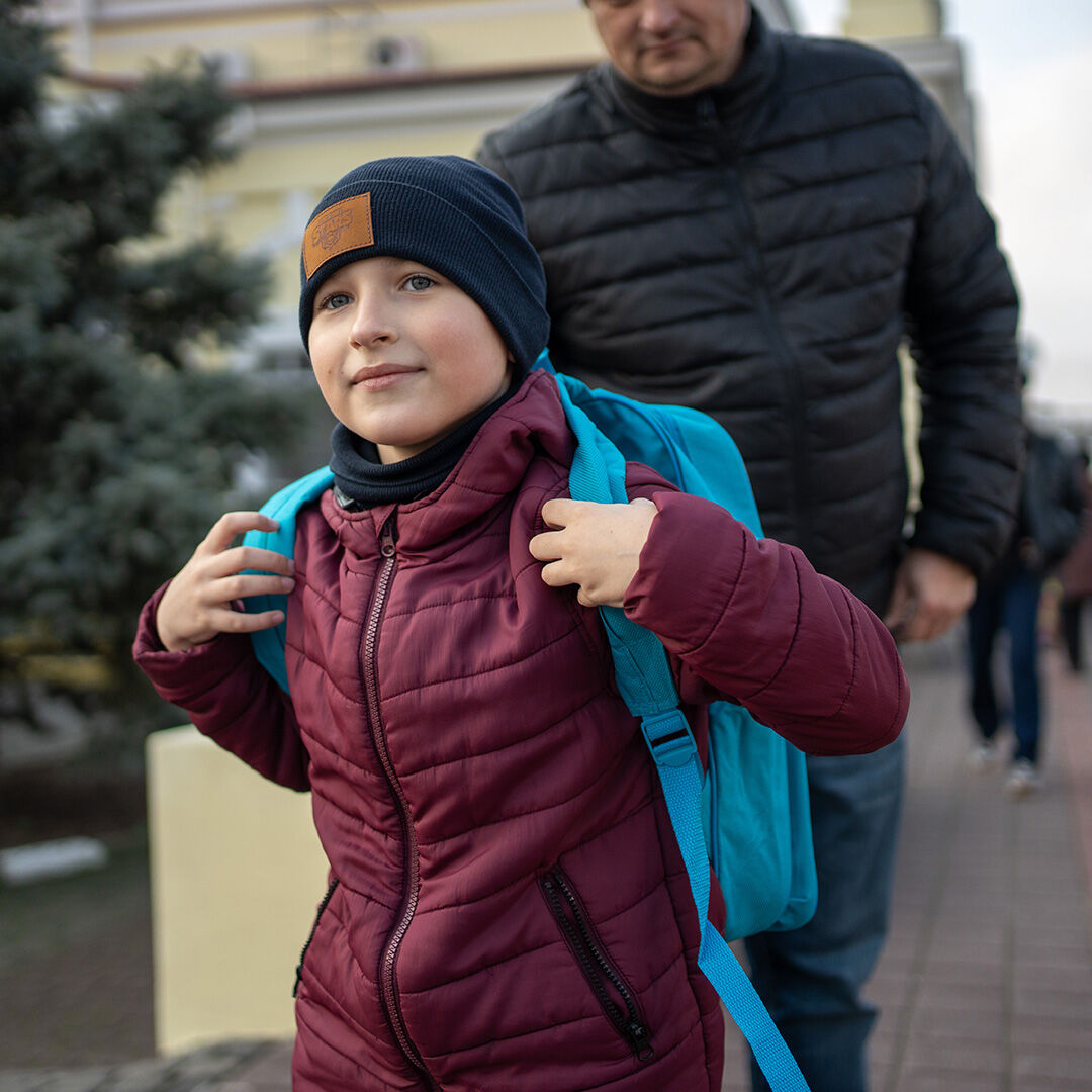 Ett ukrainskt barn med en mössa på huvudet och en UNICEF-ryggsäck på ryggen.