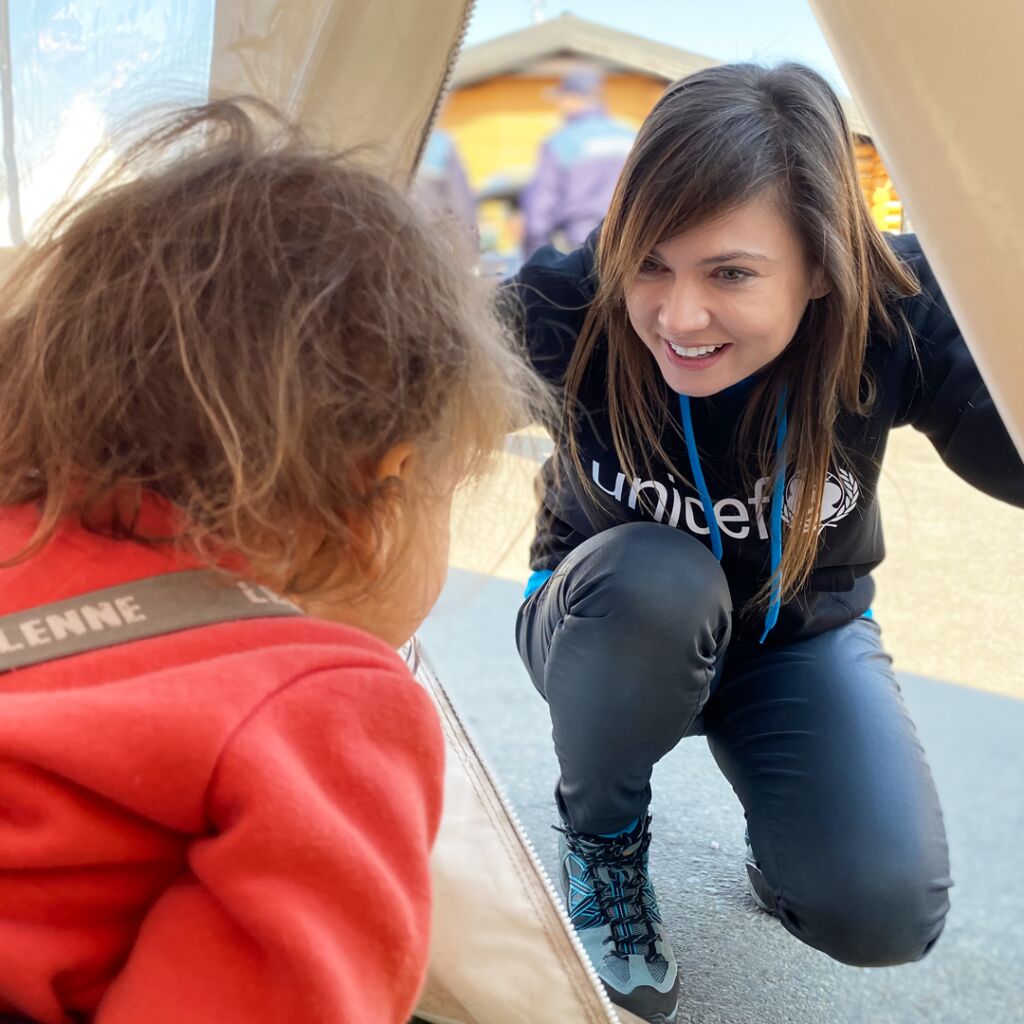 UNICEFin työntekijä kurkistaa sisälle telttaan, jossa on lapsi.