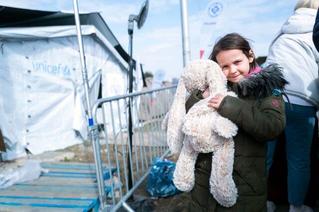 Pieni lapsi rutistaa pupupehmolelua UNICEFin teltan vieressä.