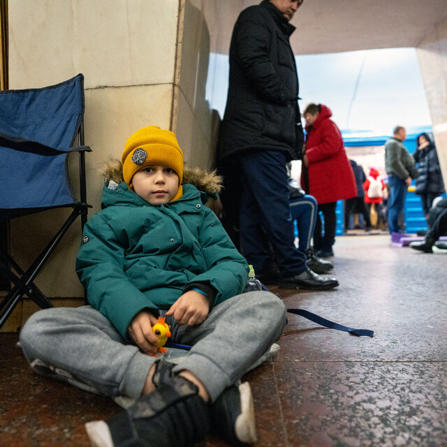 Lapsi istuu lattialla metrotunnelissa ja katsoo kameraan. 