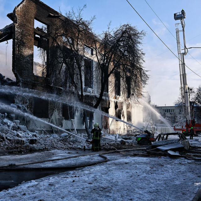 Tuhoutunut rakennus keskellä talvista maisemaa Kiovassa. Pelastajat ruiskuttavat vettä. 
