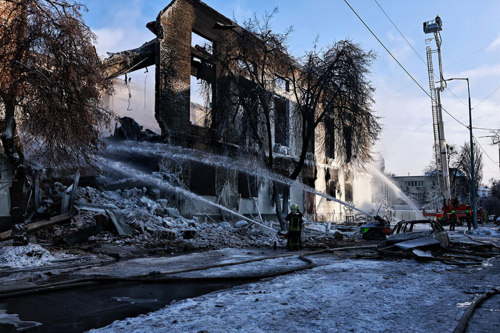 Tuhoutunut rakennus keskellä talvista maisemaa Kiovassa. Pelastajat ruiskuttavat vettä. 