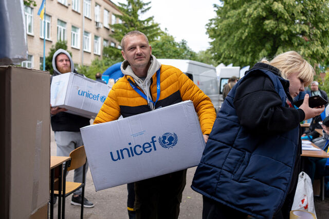 Miehet kantavat pahvilaatikoita, joissa UNICEFin logo. Taustalla pakettiauto. 