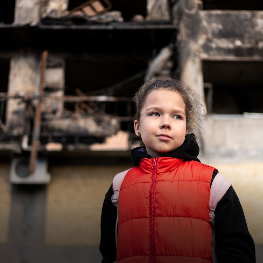 Lapsi seisoo tuhoutuneen rakennuksen edessä talvivaatteissa. 
