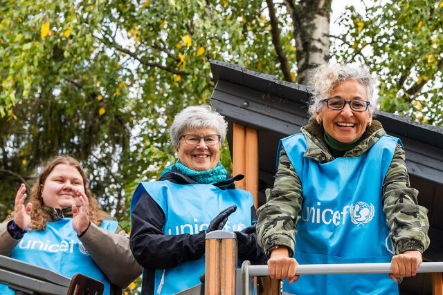 Kolme aikuista naista siniset UNICEF-liivit päällä lasten leikkitelineessä nauraa. 