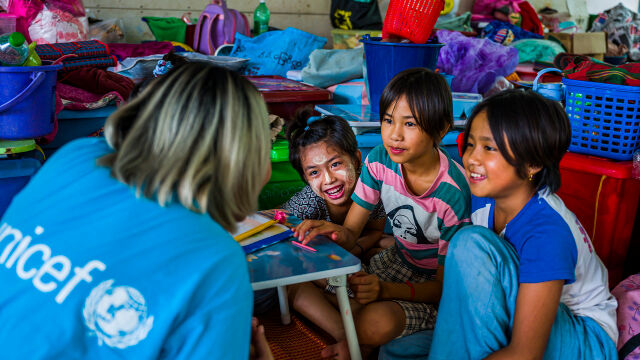 UNICEFIn työtekijä istuu lasten kanssa. Lapset nauravat. 