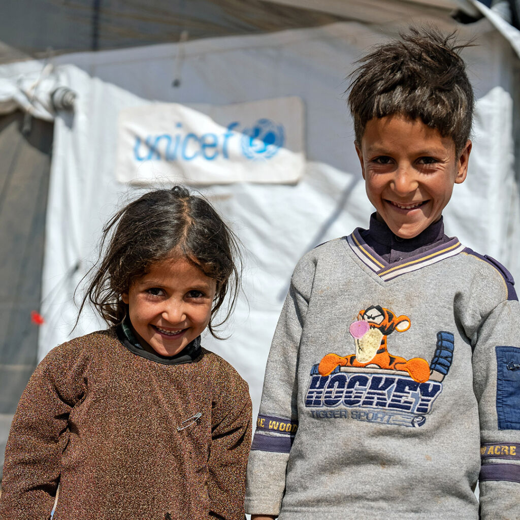 Kaksi lasta nauraa teltan edessä, jossa lukee UNICEF.