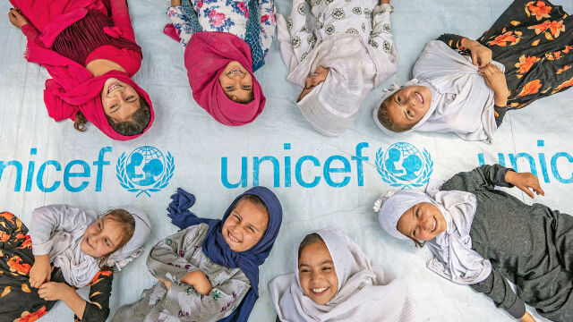Joukko noin 10-vuotiaita makaa pressun päällä, jossa lukee UNICEF ja nauraa.