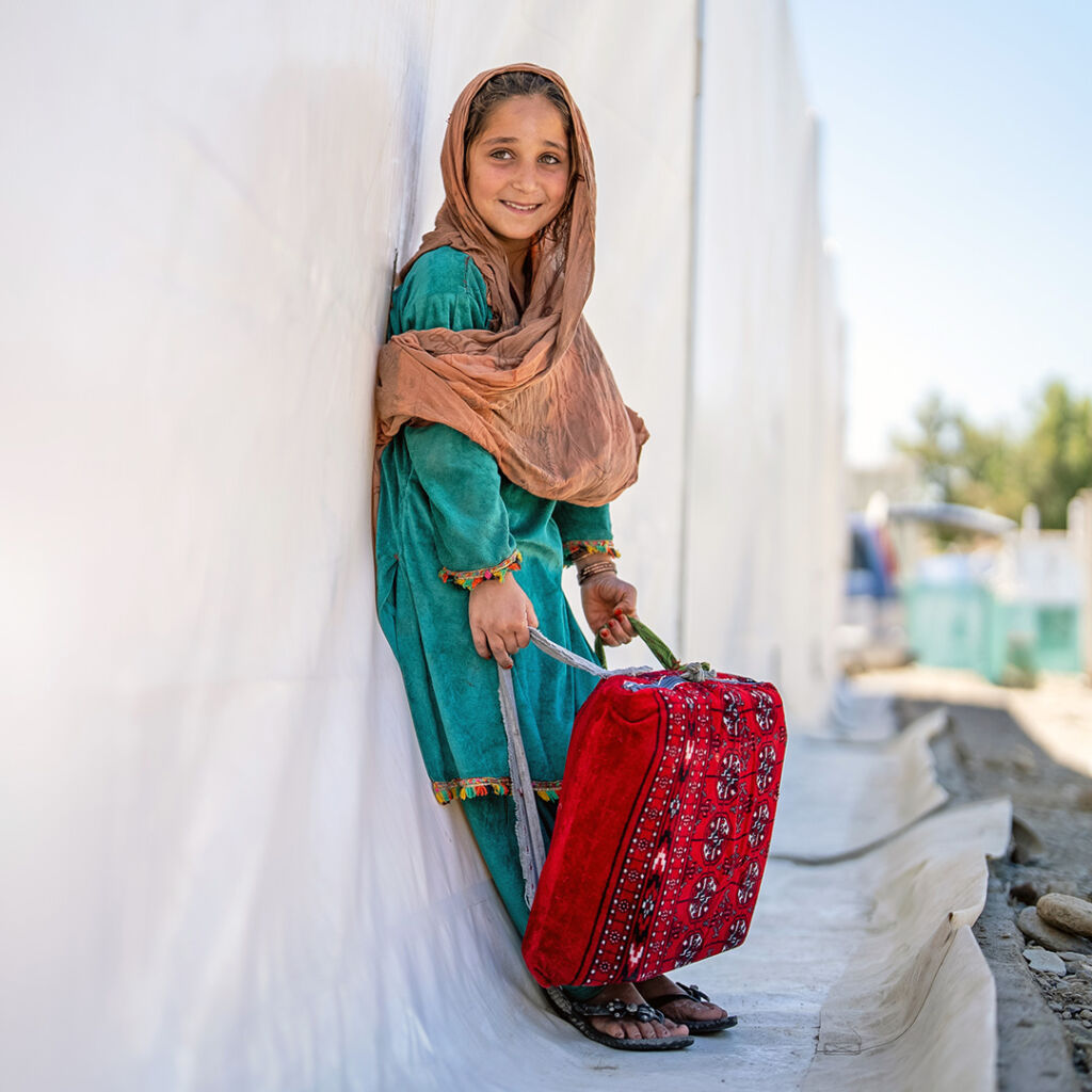 Noin kymmenenvuotias tyttö nojaa teltan seinään ja pitää kädessään reppua.