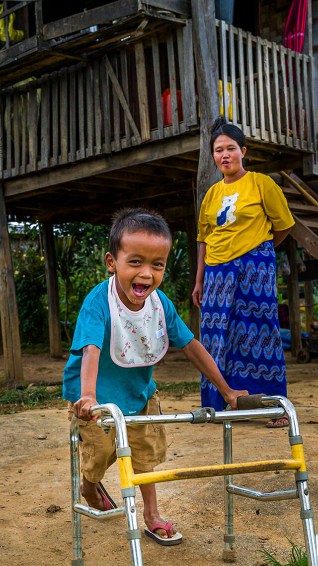 Lapsi  kävelee kävelytuen avulla ja nauraa. 